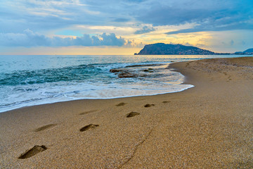 Beach, waves and footprints at sunset time.