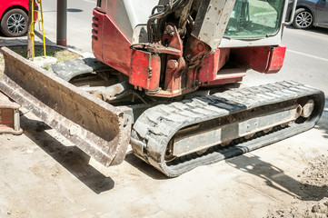 Fototapeta premium Front part of small earth mover bulldozer excavator with tracks on the street construction site prepared for work