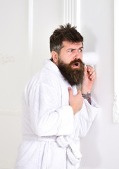 Man with beard and mustache eavesdrops using mug near wall. Hipster in bathrobe on concentrated...