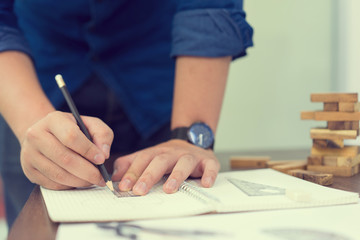 close up engineering man hand using pencil for writing or drawing plan design of construction work on sketch book page by copy from laptop concept
