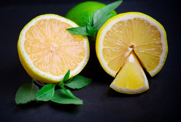 Ripe and juicy lime and lemon with a sprig of mint on a dark table