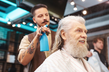 Refresh my style. Portrait of pleased bearded man that keeping smile on face and looking at the mirror