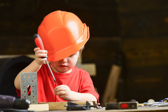 Boy play as builder or repairer, work with tools. Child dreaming about future career in architecture or building. Childhood concept. Kid boy in orange hard hat or helmet, study room background.