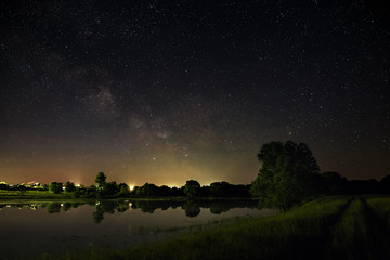 Space with stars in the night sky. The landscape with the river and trees is photographed on a long exposure. © olgapkurguzova