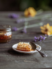 Honey with piece of honeycomb and flowers on wooden table.