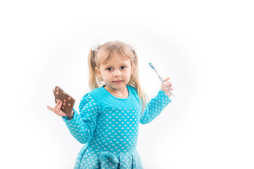 A child, a little girl is holding a toothbrush and a chocolate in her hand, a difficult choice. Diseases of children's teeth and caries.