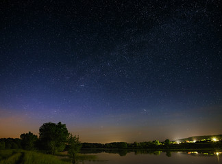 Obraz na płótnie Canvas Space with stars in the night sky. The landscape with the river and trees is photographed on a long exposure.