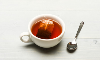 Mug filled with hot water and dipped bag of black tea. Mug filled with boiling water, teabag and spoon on white background. Tea brew concept. Process of black tea brewing in ceramic mug