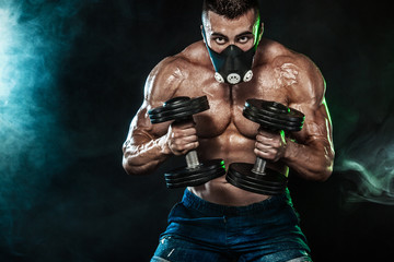 Muscular young fitness sports man, bodybuilder in training mask. Workout with dumbbell in fitness gym