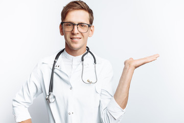 Fototapeta premium Portrait of a young doctor, on a white background, which points the hand to an empty view, trainee in the workshop, with a stethoscope on the neck, for advertising, text insertion