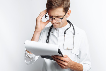 Thoughtful doctor, looking at the documents, and makes notes in the documents, a young student with a folder in his hands, on a white background, for advertising and insertion