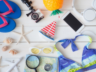 top view travel on the beach concept with action camera, map, bikini and Outfit of traveler on white wooden background, Tourist essentials, vintage tone effect