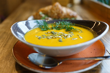  Delicious and healthy lunch: pumpkin soup with sunflower seeds and croissant with cheese on a wooden stall