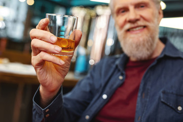 Successful adulthood. Delighted bearded male person keeping smile on face while enjoying whiskey