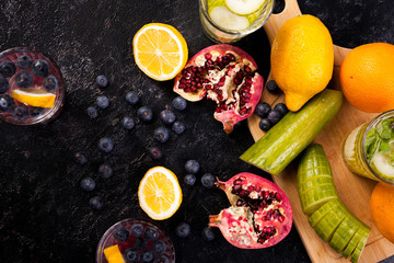 Top view of berries, pomegranate, cucumber and lemons on dark vintage wooden board