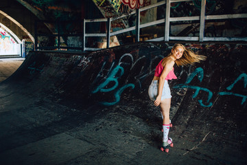 A picture of well-built rollerblaider riding backwards. She is looking back careful. Girl is smiling. Her hair is waving.