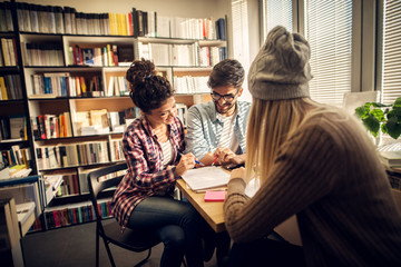 Group of joyful young students is sitting together in a library and are trying to develop solution to the problem.