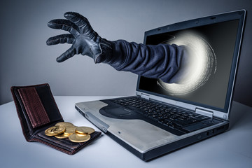 The abstract image of the hacker's hand reach through a laptop screen for stealing bitcoin in a...