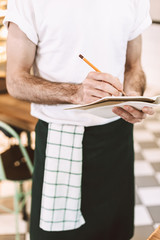 Close up photo of waiter standing with pencil and writing order in notebook in cafe