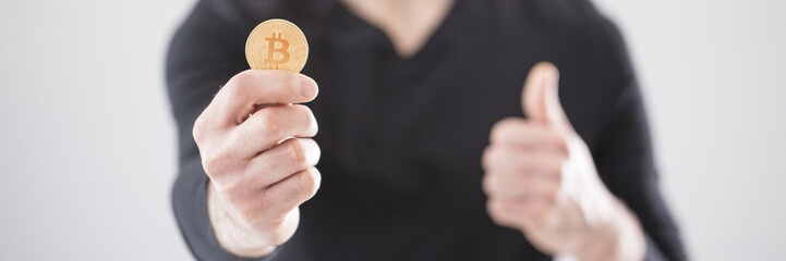 Close-up of a man holding a golden bitcoin cryptocurrency in his hand and blurry background with thumbs up pose