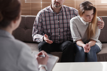 Man hugging his wife while talking to a couple therapist