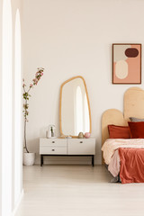 Real photo of a bedroom interior with a bed standing next to a cupboard with a mirror and a wall with a poster
