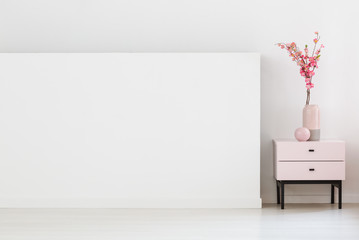 Pink flowers on cabinet next to white wall with copy space in living room interior. Real photo