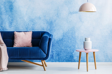 Blue and soft pink minimal style living room. Interior with dark couch, small side table and hanging lamp against ombre background. Real photo. © Photographee.eu