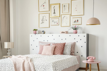 Beautiful white bedroom interior with feminine decor, polka dot pattern, pink accessories and framed sketches gallery on the wall