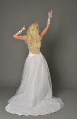 Fototapeta na wymiar full length portrait of blonde girl wearing white gown, standing pose with back to the camera. grey studio background.