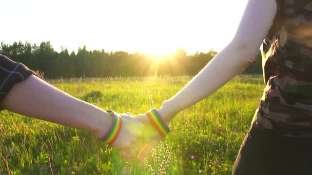 two girls walking hand in hand on the field at sunset, sun, LGBT symbol
