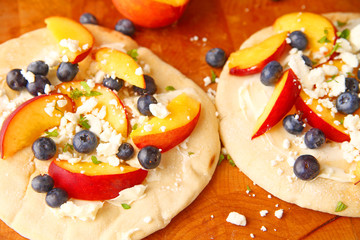 Small fruit pizzas with mascarpone, fresh blueberries and peaches with crumbled feta cheese on top
