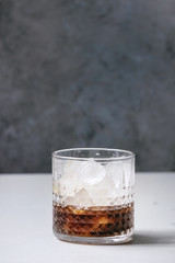 Iced coffee cocktail or frappe with ice cubes in glass on white marble table with grey concrete wall at background.
