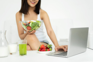 Asian woman holding healthy salad bowl while using Laptop.