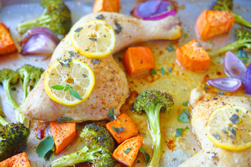 Overhead of chicken quarters with lemon, sweet potatoes, broccoli and onions