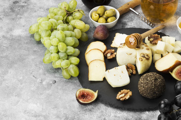 Snacks with wine - various types of cheeses, figs, nuts, honey, grapes on a gray background. Copy space. Food background