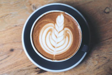 Top view image of a blue cup of hot latte coffee with latte art on vintage wooden table in cafe
