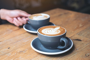 Closeup image of a hand holding blue cup of hot latte coffee on vintage wooden table in cafe