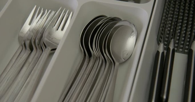 Tilt down to close-up woman's hand as she opens drawer full of stainless steel cutlery, focus on spoons. Draw closed again in kitchen. Real time 4K