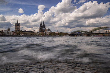 Köln Panorama mit dem Kölner Dom der Groß St. Martinskirche und der Hohenzollernbrücke, bewölkter Himmel und Wellen im Rhein