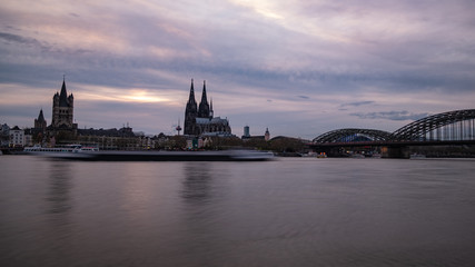 Fototapeta na wymiar Köln Panorama mit dem Kölner Dom der Groß St. Martinskirche und der Hohenzollernbrücke, bewölkter Himmel und Wellen im Rhein
