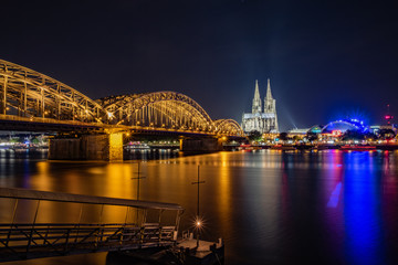 Fototapeta premium Hohenzollernbrücke, Kölner Dom und Musical Dome mit Anlegesteg für die Fähre - Panorama bei Nacht