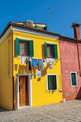 View of colorful terraced houses and clothes hanging in an alley on sunny day in Burano, a gracious little town full of canals, near Venice. Veneto region, northern Italy