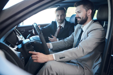 Side view portrait of mature bearded businessman sitting inside brand new car in dealership...