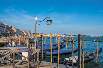 Fototapeta na wymiar Panoramic view of Venice lagoon with pier and gondolas with blue sunny sky and lamp At the city of Venice, the historic and amazing marine city. Veneto region 
