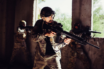 Strong and well-built soldier is standing with his opponents in dark room and guarding it. they are...
