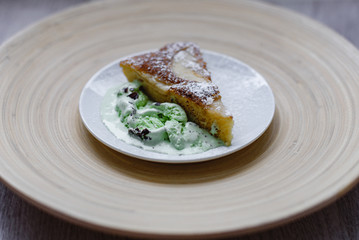 A piece of apple pie with pistachio ice cream on a background of a bamboo plate in a white plate.