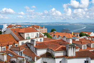 View over the red tile roofs of the Alfama district under a beautiful blue sky with puffy white clouds in Lisbon, Portugal