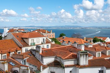 Fototapeta premium View over the red tile roofs of the Alfama district under a beautiful blue sky with puffy white clouds in Lisbon, Portugal