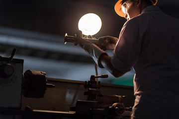 Mechanic Engineer Turner Miller verifies the accuracy of manufacturing steel parts with a scale the size of the measurement device. In the dark room with lamp background.